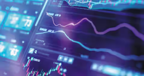 Close-up of a digital trading screen displaying multiple financial charts and graphs. The screen shows real-time market data, including line and candlestick charts, various indicators, and numerical values. The background has a blue and purple color scheme with a blurred effect.