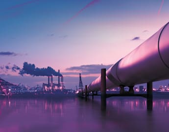 A large industrial pipeline extends over calm waters towards a distant refinery with multiple smokestacks emitting smoke. The sky is a gradient of purple and pink hues, suggesting either dawn or dusk, and the scene is bathed in a soft, diffused light.