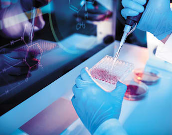 A gloved scientist uses a pipette to add liquid to a 96-well plate in a laboratory. Scientific equipment and a computer screen displaying chemical formulas are visible in the background, highlighting a research environment.