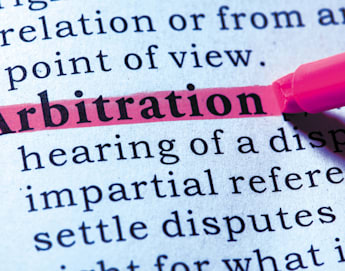 A close-up of a dictionary page with the word "Arbitration" highlighted in pink. The definition and surrounding text are slightly blurred, while the word "Arbitration" is sharp and clear, emphasizing its importance. A pink highlighter marker is visible nearby.