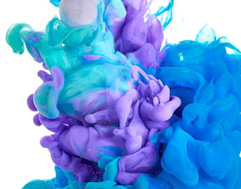 A vibrant swirl of purple, turquoise, teal, and blue ink disperses in clear water against a white background, creating an abstract and vivid display of color blending and fluid motion.