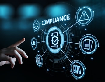 A hand reaches towards a digital interface displaying the word "COMPLIANCE" at the center. Surrounding icons represent various compliance aspects like warning signs, documents, and user profiles, all connected by futuristic lines and circles against a dark background.