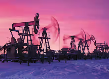 Oil pumps silhouetted against a striking pink and purple sky at sunset or sunrise. Snow covers the ground, while the pumps, in varying positions, appear to be in motion. The scene captures an industrial landscape amid a serene, wintry atmosphere.