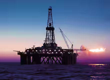 An offshore oil drilling platform is illuminated against a twilight sky over the ocean. A large flame is visible on the right side of the platform, suggesting gas flaring. A crane extends from the platform, and the sea is calm beneath.