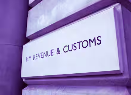 A stone building with a sign reading "HM Revenue & Customs" in capital letters is displayed in dark text on a light background. The sign is affixed to the wall with engraved lettering, indicating the government department responsible for tax and customs operations.