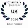 A blue laurel wreath surrounds the text: "Chambers Ranked In UK 2026" with the name "Eman Hassan" below, indicating a ranking recognition.