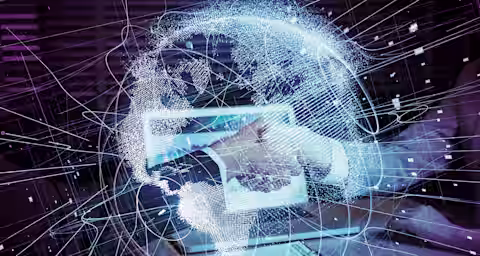 A futuristic image showing a person using a tablet. Surrounding the tablet and their hand are glowing, intricate digital lines and nodes forming a virtual network or globe, suggesting connectivity and advanced technology. A document with charts is on the table.