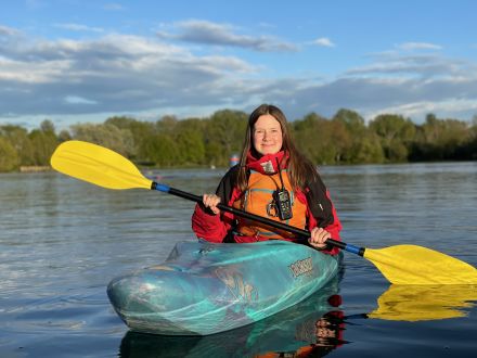 dark haired young woman in bright blue kayak with yellow paddle on Stanborough Lake