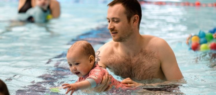 A parent helping his toddler float in a swimming lesson.