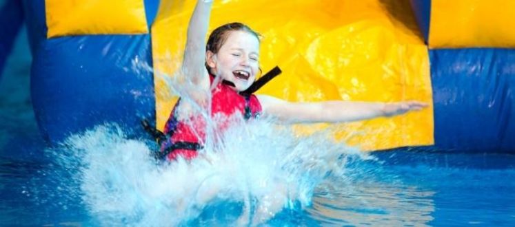 A laughing child splashing into the water down a pool inflatable slide