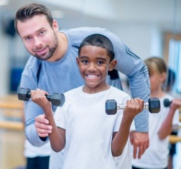 Junior fitness class - instructor with boy using hand weights