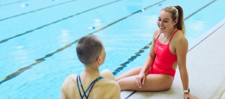 image shows two ladies sitting and smiling each other on the edge of a pool