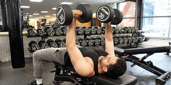 A man working out in the Free Weights Area at Sugden gym using dumbells and bench