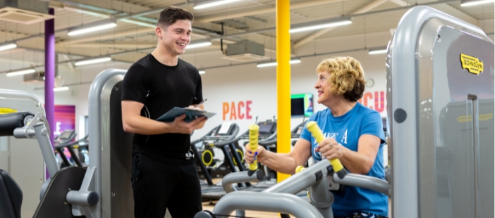 image shows a female on gym equipment with an instructor advising her