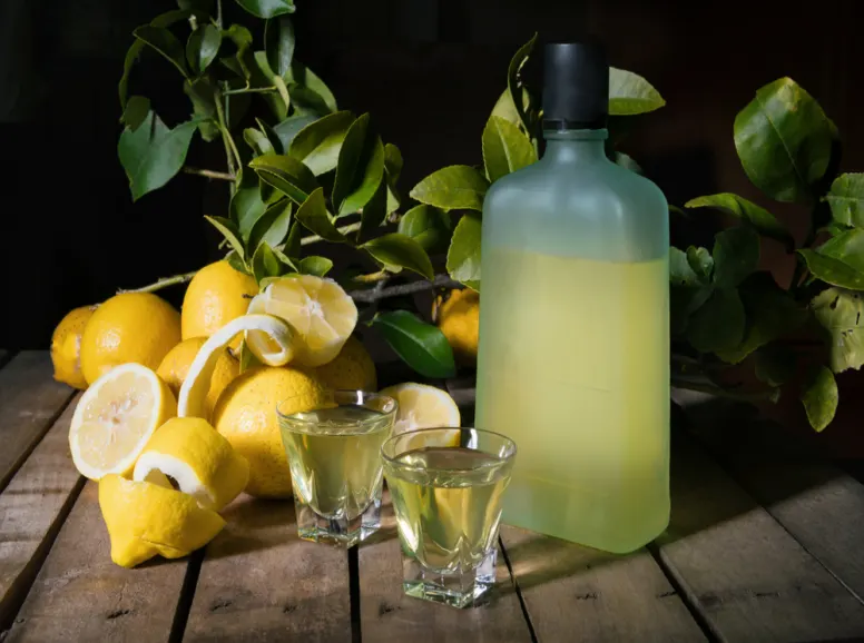 Lemons and Shot Glasses Next to a Bottle of Limoncello