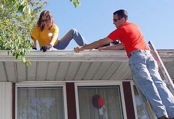 Man on a ladder and woman on roof of house, either installing or cleaning the gutters