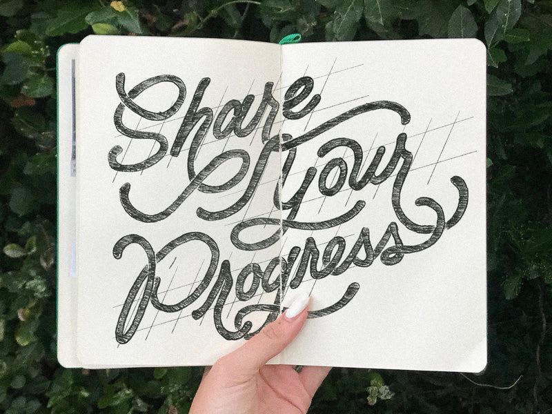 A notebook open in someone's hand, upon which is written, "Share Your Progress"