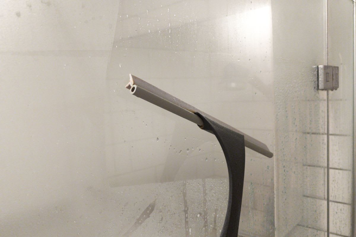 Ein Duschabzieher wird benutzt, um Kalkablagerungen an einer Duschwand vorzubeugen.