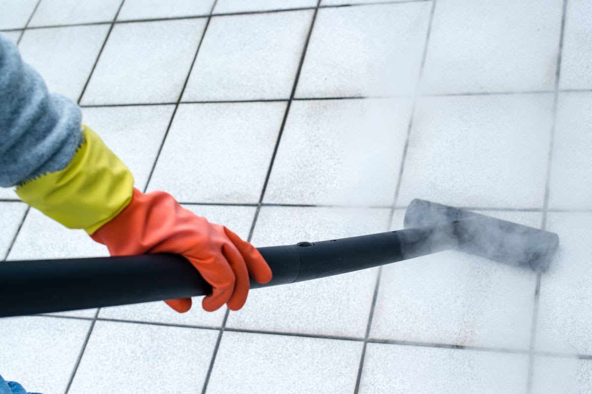 Person verwendet einen Dampfreiniger, um Bodenfliesen zu reinigen, wobei Dampf sichtbar ist.