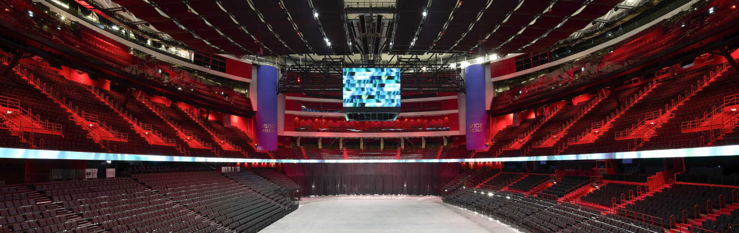 Interior view of an empty sports arena with red seating and a large video screen hanging from the ceiling.