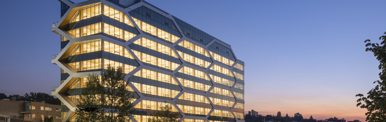 Modern multi-story office building with a geometric, honeycomb-patterned facade illuminated at dusk.