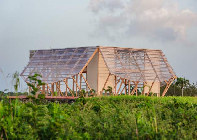 Modern wooden pavilion with a slatted roof in a grassy field under a cloudy sky.