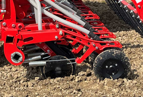 Close-up of a Kverneland CX II seed drill coulter system working in tilled soil, showing red discs and seed tubes for precise planting.