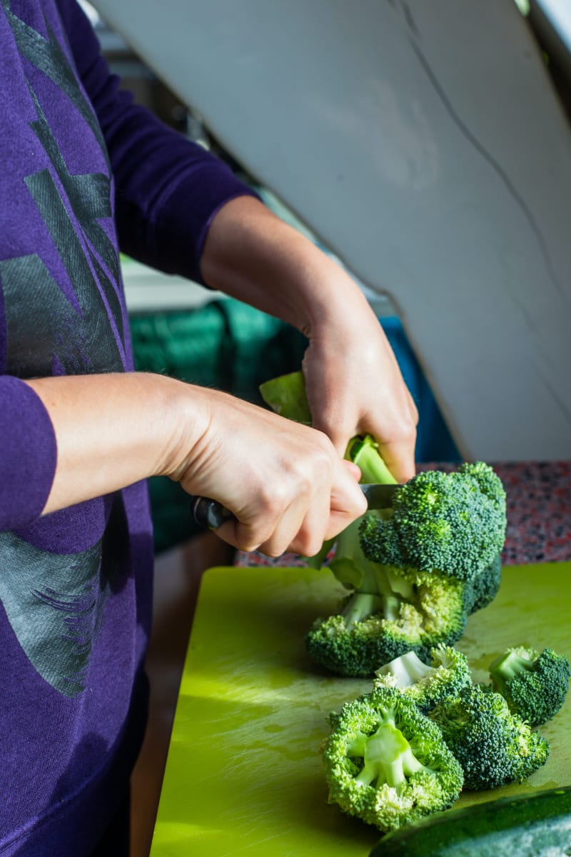 person cutting off broccoli florets from head of broccoli on green cutting board