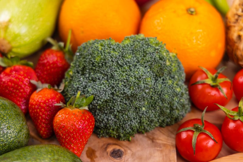 broccoli, strawberries, tomatoes, oranges on a wood cutting board