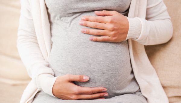 Close-up of young pregnant woman touching her abdomen while sitting on the couch