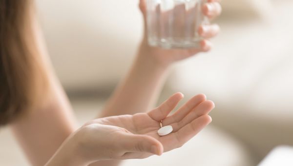 someone holding a white pill in one hand and a glass of water in another