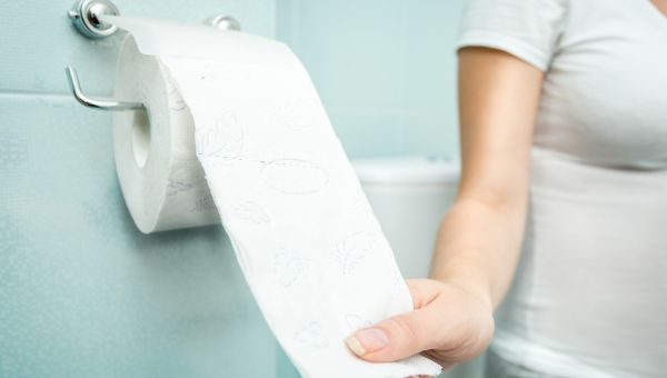 Pregnant person sitting on the toilet and reaching for the toilet paper