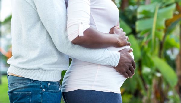 a pregnant person standing with another person who is standing behind them and placing hands on their stomach
