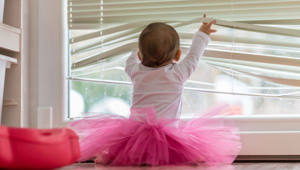 Toddler wearing pink tutu opening up blinds and staring out of window