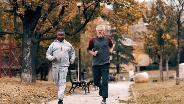 Two older men jogging in park in fall.