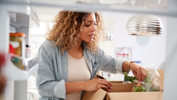 Woman opening delivery box of groceries near fridge