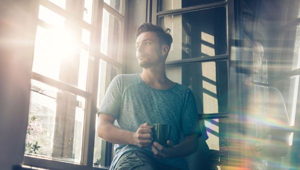 Young man holding coffee cup and looking out of window.