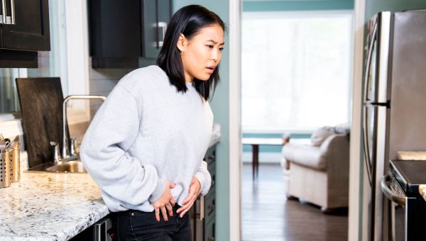 Woman holding her stomach in pain in the kitchen.