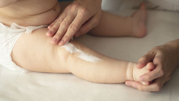 parent rubbing moisturizing cream on baby's leg