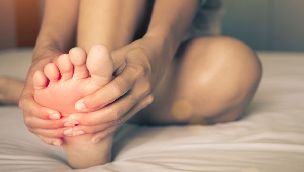 woman grabs foot while on bed.