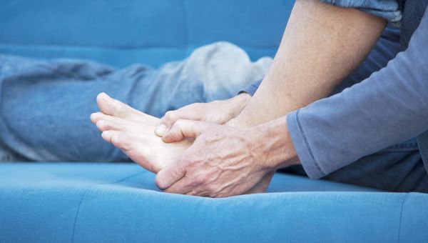 Man massaging foot pain on blue couch