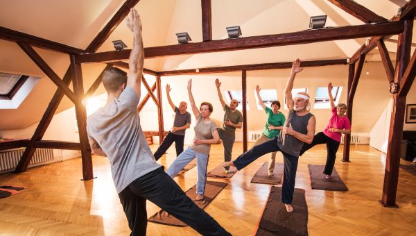 a group of older adults does a yoga class under the instruction of a yoga teacher