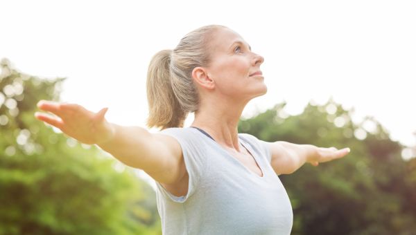 a middle aged white woman spreads her arms in a yoga pose and looks to the sky