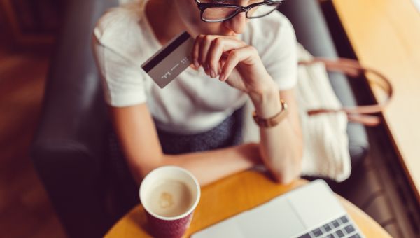 person looking thoughtful, holding credit card, looking at laptop