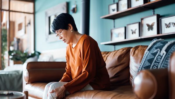 a mature Asian woman with leg pain sits on her couch