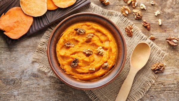 A bowl of mashed sweet potatoes with chunks of walnuts.