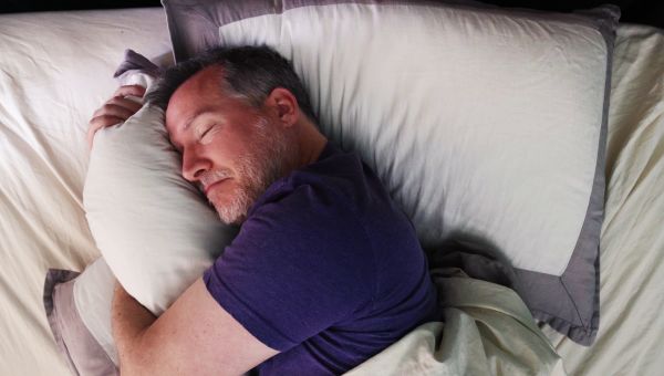 a middle aged man sleeps soundly in bed while hugging a pillow