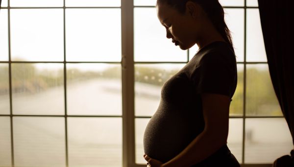 A pregnant woman with bipolar disorder holding her belly and thinking in front of a window