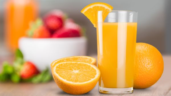 a tall glass of orange juice on a countertop with a sliced orange