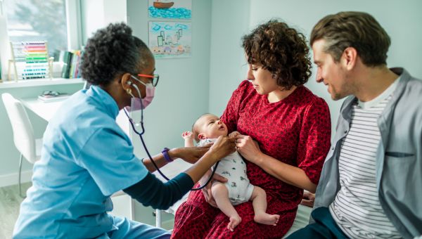 a mother and father hold their baby at an appointment with a pediatrician